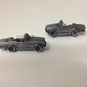 May include: A pair of silver-colored miniature convertible car cufflinks. The cars have black wheels and a white interior.