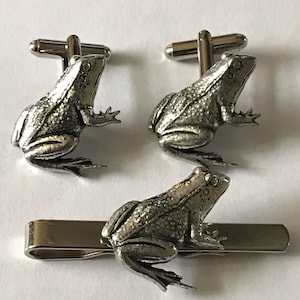 May include: A set of silver frog cufflinks and a tie clip. The frogs are detailed with textured skin and have a realistic appearance.