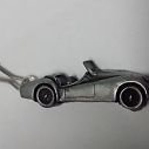 May include: A silver-colored metal keychain charm shaped like a classic British sports car. The car is a convertible with a black interior and black wheels.
