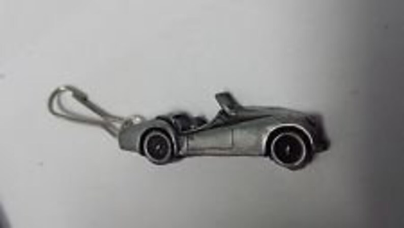 May include: A silver-colored metal keychain charm shaped like a classic British sports car. The car is a convertible with a black interior and black wheels.