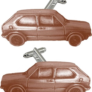 May include: A pair of cufflinks featuring a detailed miniature replica of a classic car. The car is a brown color and has a silver-toned metal base.