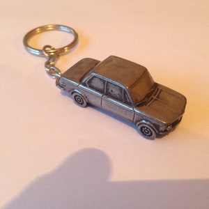 May include: A silver metal keychain featuring a detailed model of a classic BMW car.