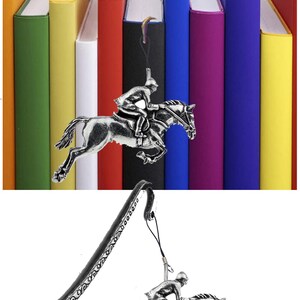 May include: A silver bookmark featuring a detailed sculpture of a horse and rider jumping over a fence. The bookmark has a long, curved tail with an ornate design. The bookmark is displayed against a background of colorful books.