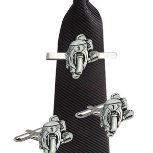 Könnte beinhalten: Eine schwarze Krawatte mit einer silbernen Motorrad-Krawattenklammer und passenden Manschettenknöpfen. Die Krawattenklammer und die Manschettenknöpfe zeigen ein detailliertes Motorrad-Design mit der Nummer 1. Die Krawatte hat eine gerippte Textur.