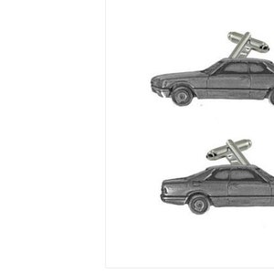 Könnte beinhalten: Ein Paar Manschettenknöpfe mit einem Zinnmodell eines Oldtimers. Die Manschettenknöpfe sind silberfarben und haben ein klassisches Design.