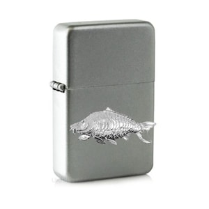 May include: A silver lighter with a detailed engraving of a carp fish.