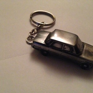 Puede incluir: Un llavero de coche plateado con un diseño detallado. El llavero está unido a un anillo plateado.