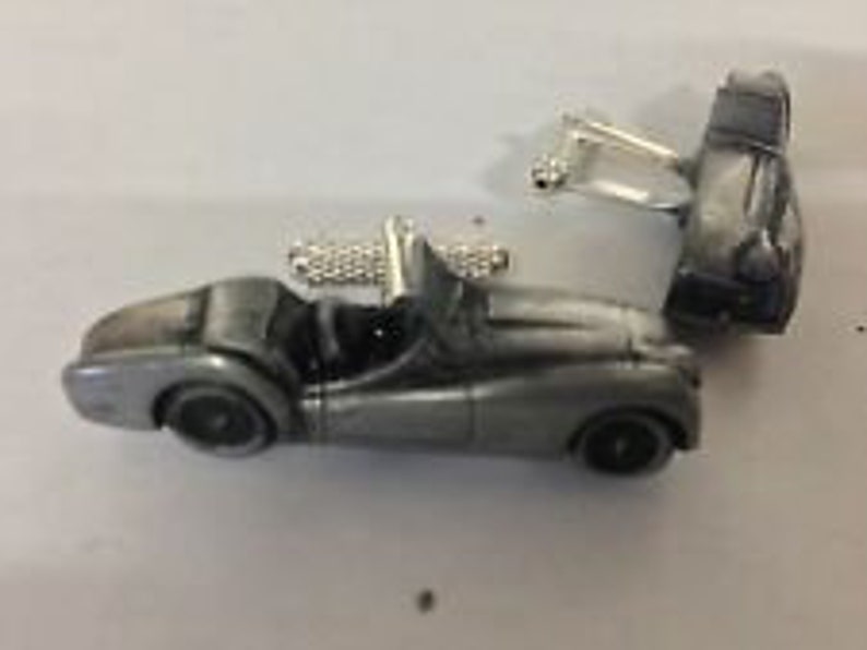 May include: A pair of silver cufflinks featuring a detailed miniature model of a classic sports car.