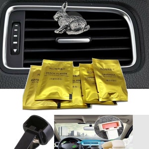 May include: A set of car vent clips with a silver rabbit figurine. The clips are black and come with four small gold pouches containing air fresheners. The pouches have Chinese text and English text that reads "Peach Flavor", "Lemon", and "Lavender".