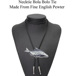 Puede incluir: Un bolo tie de plata con forma de pez en un expositor negro. La corbata está hecha de fino estaño inglés. "Check out my range of Necklace Necktie Bola Bolo Tie Made From Fine English Pewter" está escrito encima del expositor.