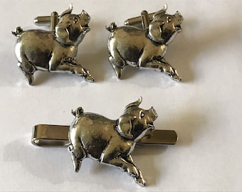 May include: A set of silver pig cufflinks and a tie clip. The pig is depicted in a running pose with its mouth open.