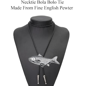 Puede incluir: Un collar bolo de pescado plateado con cordón trenzado negro. El collar se muestra en un busto de maniquí negro. El texto "Check out my range of Necklace Necktie Bola Bolo Tie Made From Fine English Pewter" está por encima de la imagen.