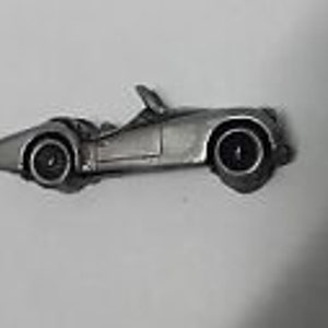 May include: A silver-colored pewter model of a classic convertible sports car. The car has a black windshield and black wheels.