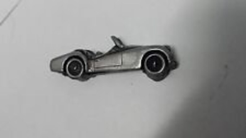 May include: A silver-colored pewter model of a classic convertible sports car. The car has a black windshield and black wheels.