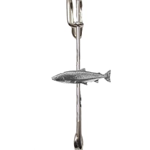 Puede incluir: Un broche plateado con un diseño detallado de pez. El pez está posicionado horizontalmente a través del eje del alfiler. El alfiler tiene un diseño clásico de imperdible con una parte superior en bucle y un cierre seguro.