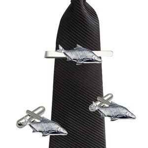 Puede incluir: Una corbata negra con un clip de corbata plateado y gemelos con un diseño de pescado.