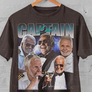 May include: Dark brown t-shirt featuring a graphic of five men, with the word "CAPTAIN" in a teal font. The men are wearing sunglasses and formal attire. The shirt is hanging on a wooden hanger.