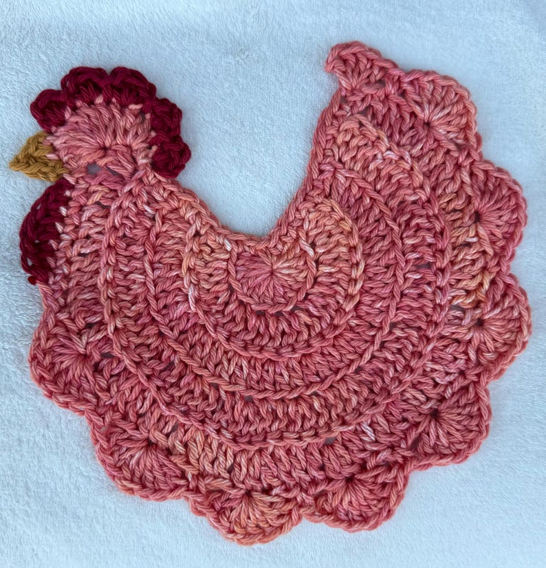 May include: A crocheted pink and red chicken dishcloth with a scalloped edge.