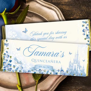 May include: Two chocolate bar wrappers with a light blue floral design and text. One wrapper says "Thank you for sharing this special day with us." The other says "Tamara's Quinceañera" with a date and a castle illustration.