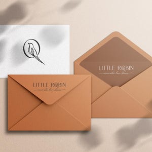 May include: A brown envelope with the text "LITTLE ROBIN - minimalist fine jewelry" printed on the front. The envelope is sitting on a beige surface.