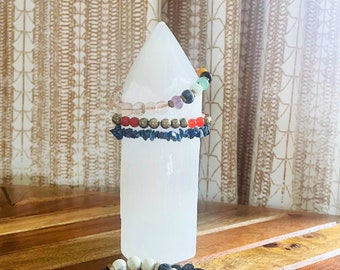 Könnte beinhalten: Eine Sammlung von Armbändern mit Perlen in verschiedenen Farben und Designs. Einige Armbänder werden auf einem weißen, zylindrischen Objekt präsentiert. Andere Armbänder befinden sich auf einer Holzoberfläche. Die Armbänder haben Edelsteine, Perlen und Metallakzente.