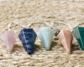 Puede incluir: Seis péndulos de cristal de varios colores, incluyendo rosa, azul, verde y marrón, están enhebrados en una cadena plateada. Los péndulos tienen todos la forma de una pirámide.
