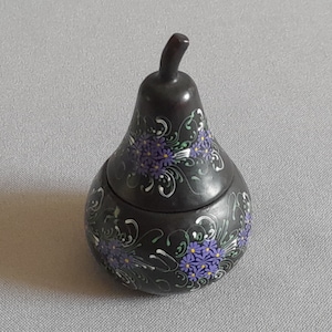 May include: A black pear-shaped ceramic trinket box with a lid, decorated with hand-painted purple flowers and green leaves.