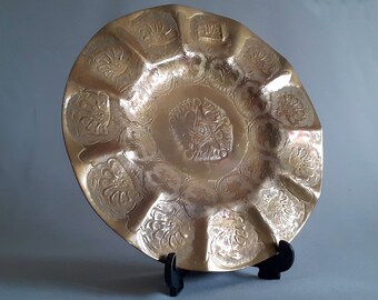 May include: A decorative brass serving dish with a scalloped edge and intricate floral designs. The dish has a slightly raised center and a smooth, polished finish.