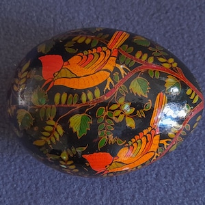 May include: Black egg-shaped trinket box with a painted design of two orange and red birds perched on branches with green leaves.
