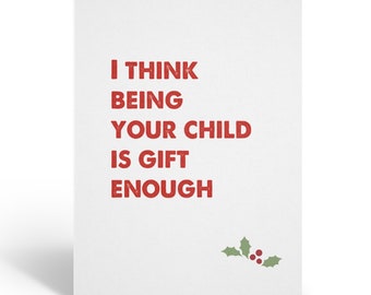 Puede incluir: Una tarjeta de felicitación blanca con el texto "I THINK BEING YOUR CHILD IS GIFT ENOUGH" en rojo. Una pequeña ramita de acebo con bayas rojas está en la esquina inferior derecha. La tarjeta está doblada y de pie.