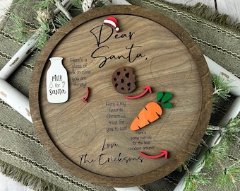 Op de afbeelding: Een ronde houten dienblad met een kerstman-thema. Het heeft een melkfles, een koekje, een wortel en de tekst "Beste Kerstman, Dit is mijn favoriete kersttraktatie voor jou! Met liefde, De Ericksons".