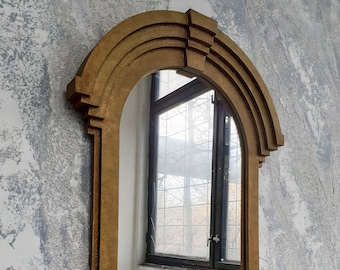 May include: A gold-colored arched mirror with a decorative frame. The mirror reflects a window with a view of trees outside.
