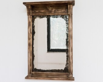 May include: A rustic wooden framed mirror with a distressed glass pane. The mirror has a dark brown wood frame with a simple design.
