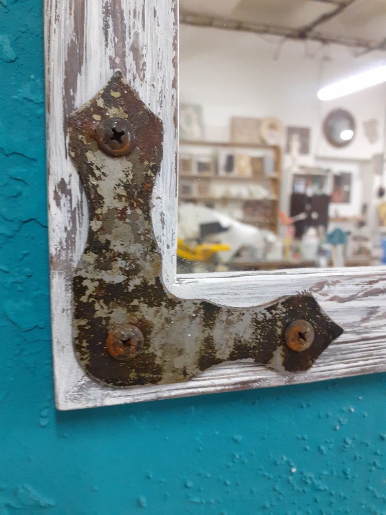 May include: A whitewashed wooden frame with a distressed finish, featuring a metal corner brace with visible rust and screws. The frame is against a teal background.