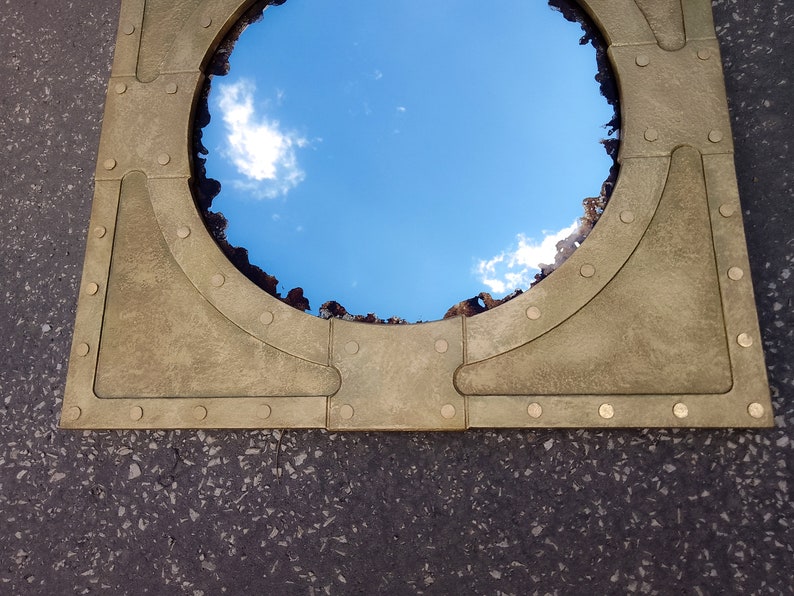 May include: A round mirror with a brass frame and rivets. The mirror reflects a blue sky with white clouds.
