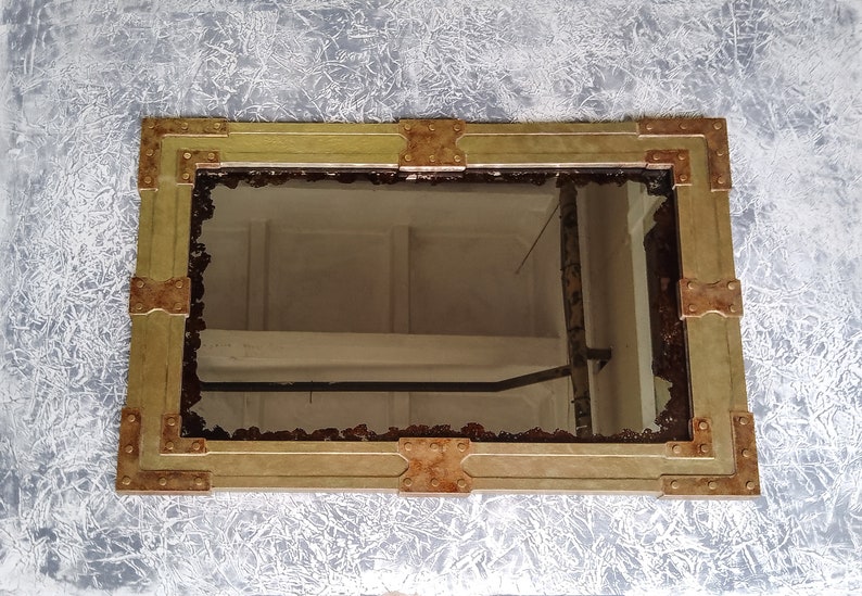 May include: A rectangular mirror with a gold frame and copper accents. The frame has a distressed look and is decorated with rivets.