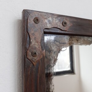 May include: A rustic wooden mirror with a distressed, brown finish. The mirror has a metal frame with three visible screws. The frame is decorated with a rusty patina.