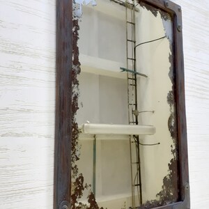 May include: A rectangular mirror with a distressed wooden frame and metal accents. The mirror has a chipped and aged look, giving it a vintage feel.