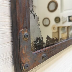 May include: A rustic wooden framed mirror with a distressed, aged, and chipped silver mirror. The frame is made of dark wood with rusty metal accents and screws.