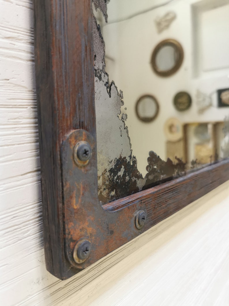 May include: A rustic wooden framed mirror with a distressed, aged, and chipped silver mirror. The frame is made of dark wood with rusty metal accents and screws.