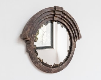May include: A round, antique-style mirror with a distressed, brown metal frame. The frame has a geometric design with multiple layers of metal.