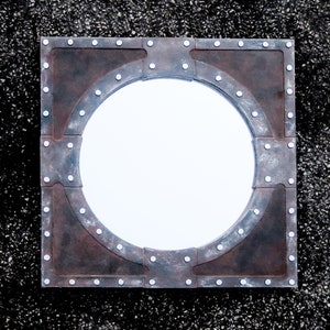 May include: A round mirror with a rustic, industrial-style frame. The frame is made of metal and has a distressed, aged look. The mirror is surrounded by a series of rivets.