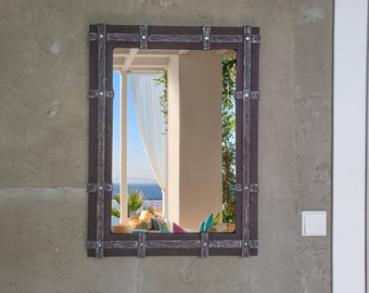 May include: A rectangular mirror with a dark brown wooden frame and metal accents. The mirror reflects a view of a patio with white curtains and a glimpse of the ocean.