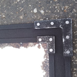 May include: A corner of a black frame with a distressed silver finish. The frame has a white background and is made of wood. The frame is decorated with silver metal corner pieces.