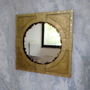 May include: A round mirror with a gold-toned frame. The frame has a unique design with rivets and a square shape.