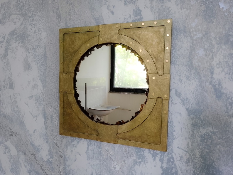 May include: A round mirror with a gold-toned frame. The frame has a unique design with rivets and a square shape.