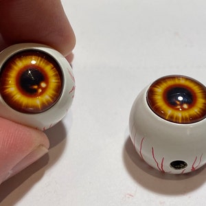 May include: Two white plastic eyeballs with red veins and brown irises. The eyeballs are about 1 inch in diameter.