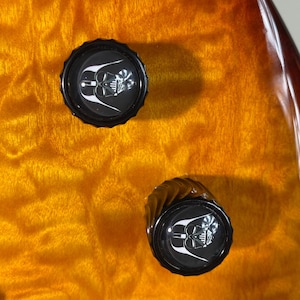 May include: Two black knobs with a white Darth Vader graphic on a brown wooden surface.
