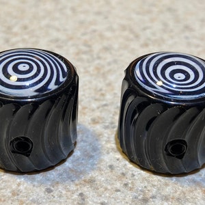 May include: Two black guitar knobs with a swirling black and white pattern on the top.