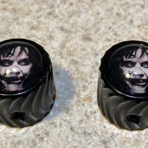 May include: Two black guitar knobs with a white and gray image of a creepy smiling face on each knob.